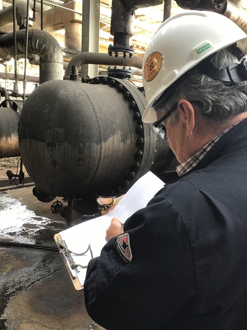 Engineer in a white helmet inspecting a flange with a clipboard